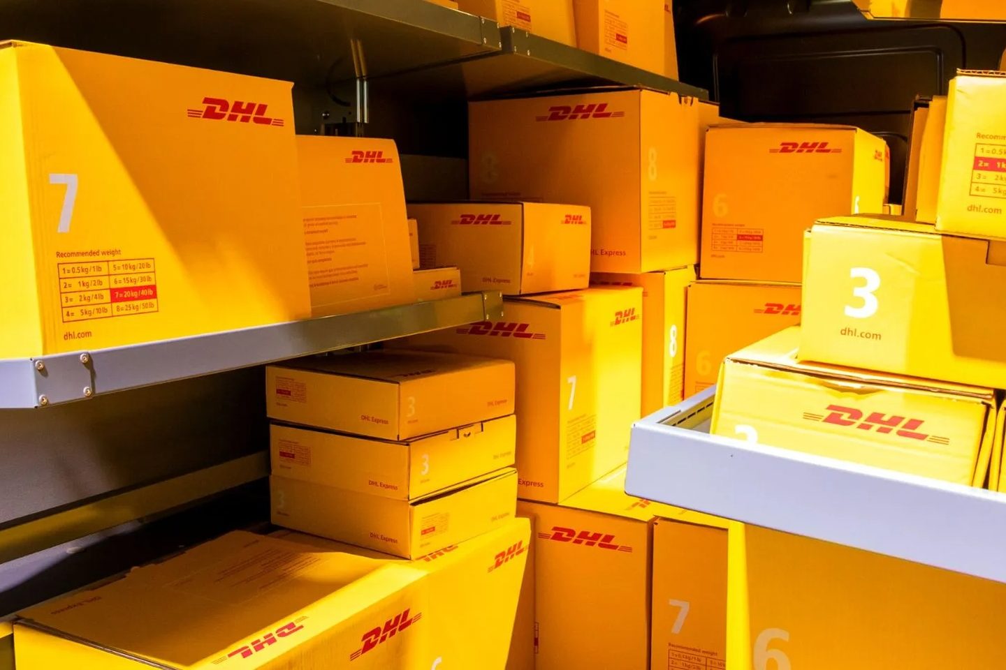 Stacked yellow DHL parcels with weight labels in a warehouse — shipping to the Canaries