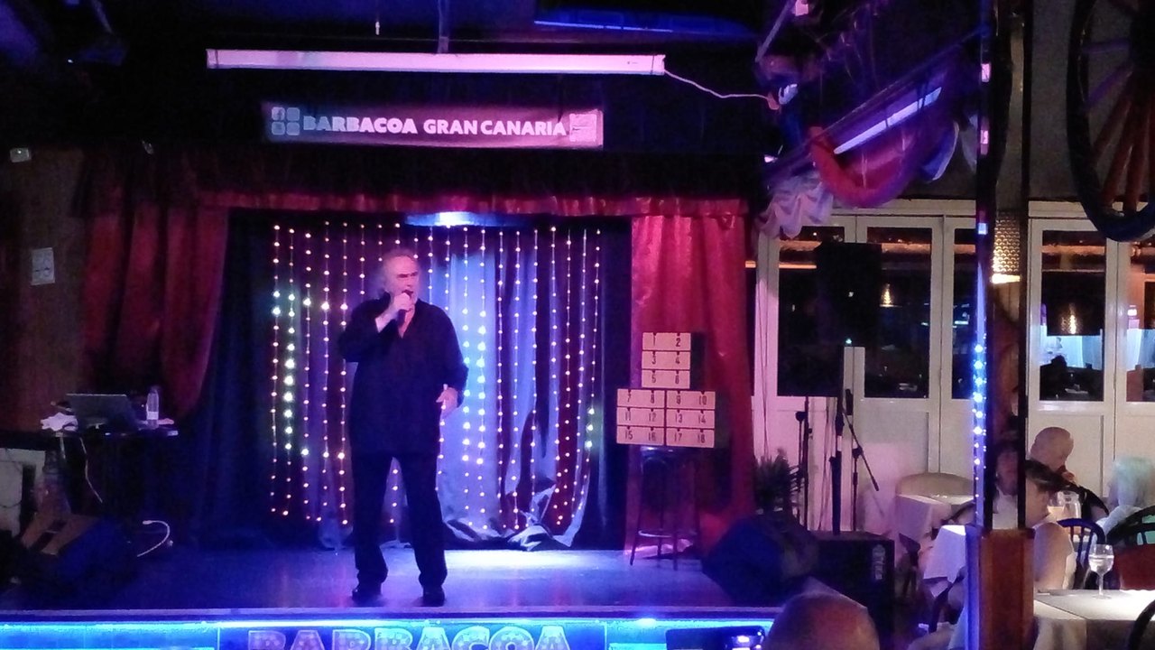 Ein Sänger auf der beleuchteten Bühne der Barbacoa-Showbar in Puerto Rico, Publikum an den Tischen