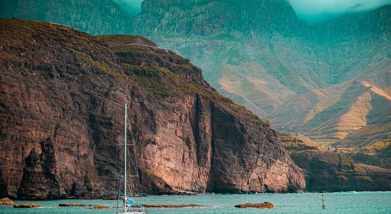 Segelboot vor steiler Felsküste auf den Kanarischen Inseln, türkisfarbenes Wasser