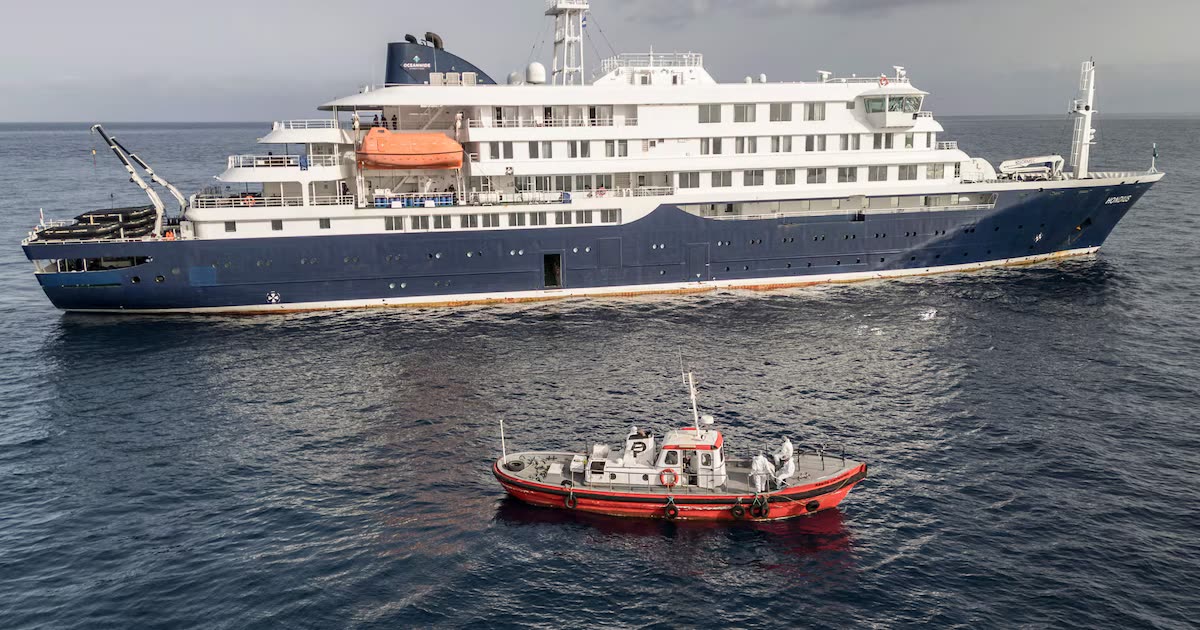MV Hondius at anchor with a pilot boat alongside, crew in protective suits