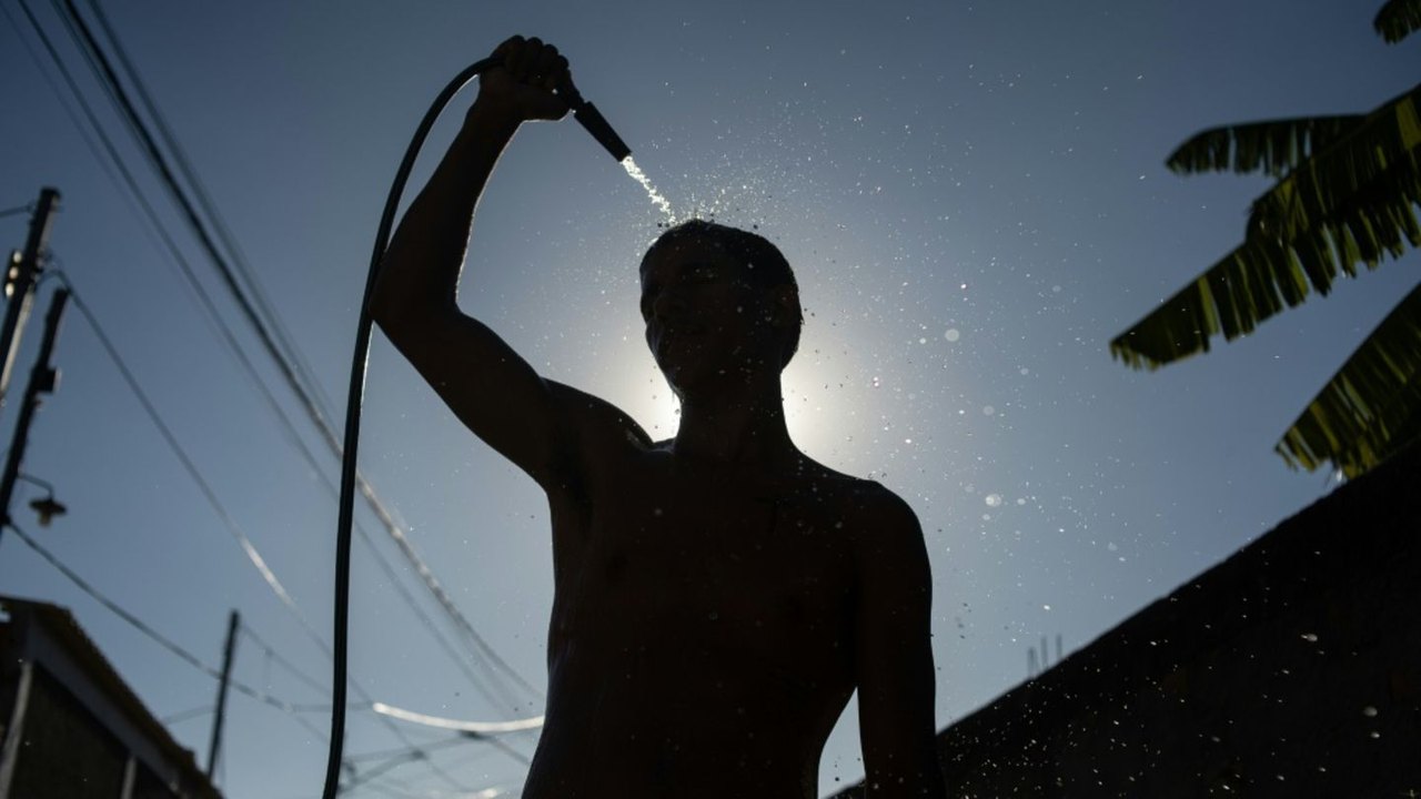 Silhouette einer Person, die sich mit einem Gartenschlauch im Gegenlicht der Sonne kühlt