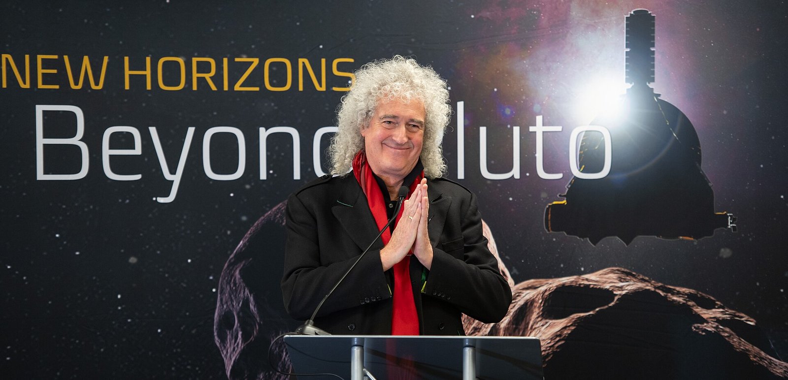 Sir Brian May performing on stage with a telescope in the background