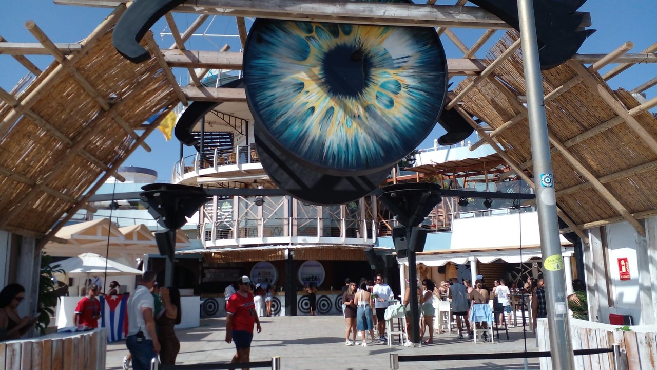 Das grosse Augen-Logo des Beachclubs Mama Juana in Meloneras, Gäste und kubanische Flagge