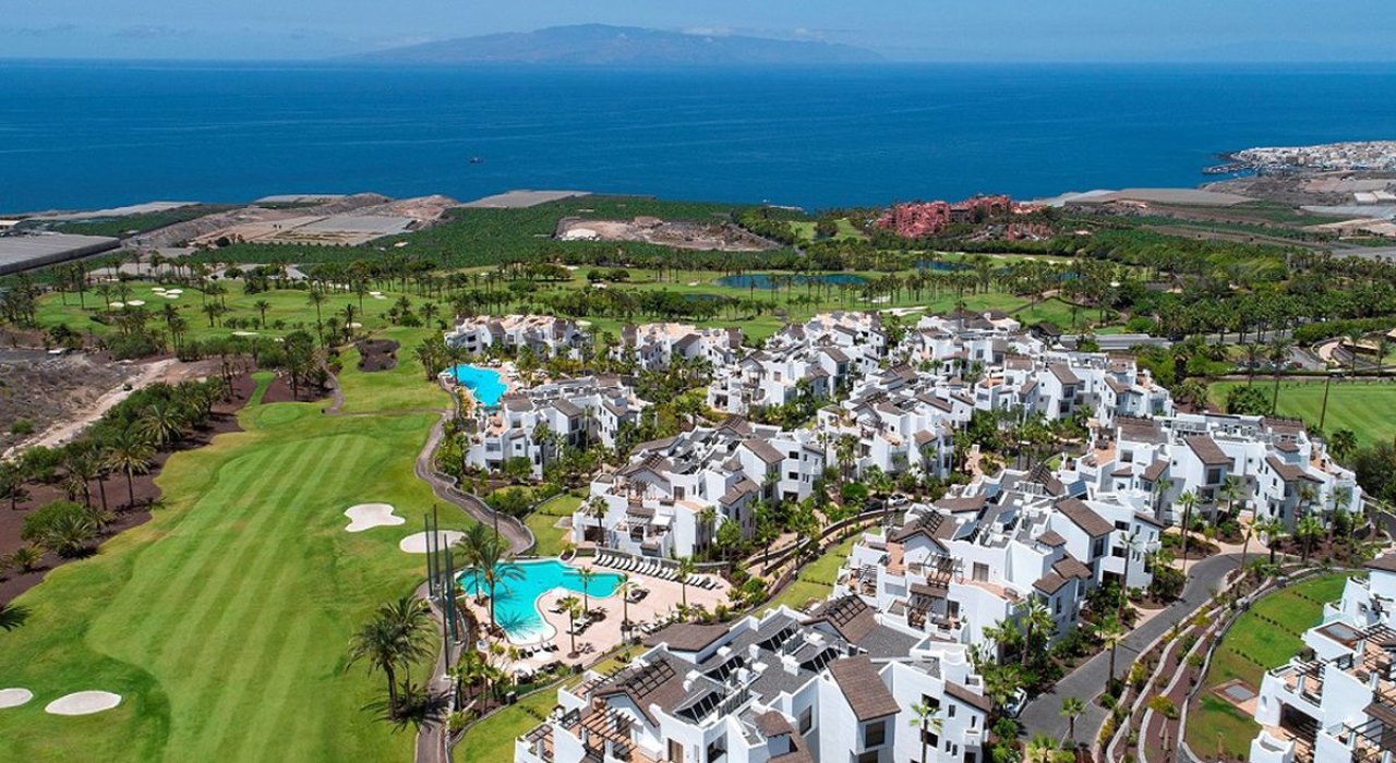 Aerial view of an apartment complex in southern Tenerife with golf course, pools and La Gomera in the distance — a symbol of the tourism infrastructure displacing local residents
